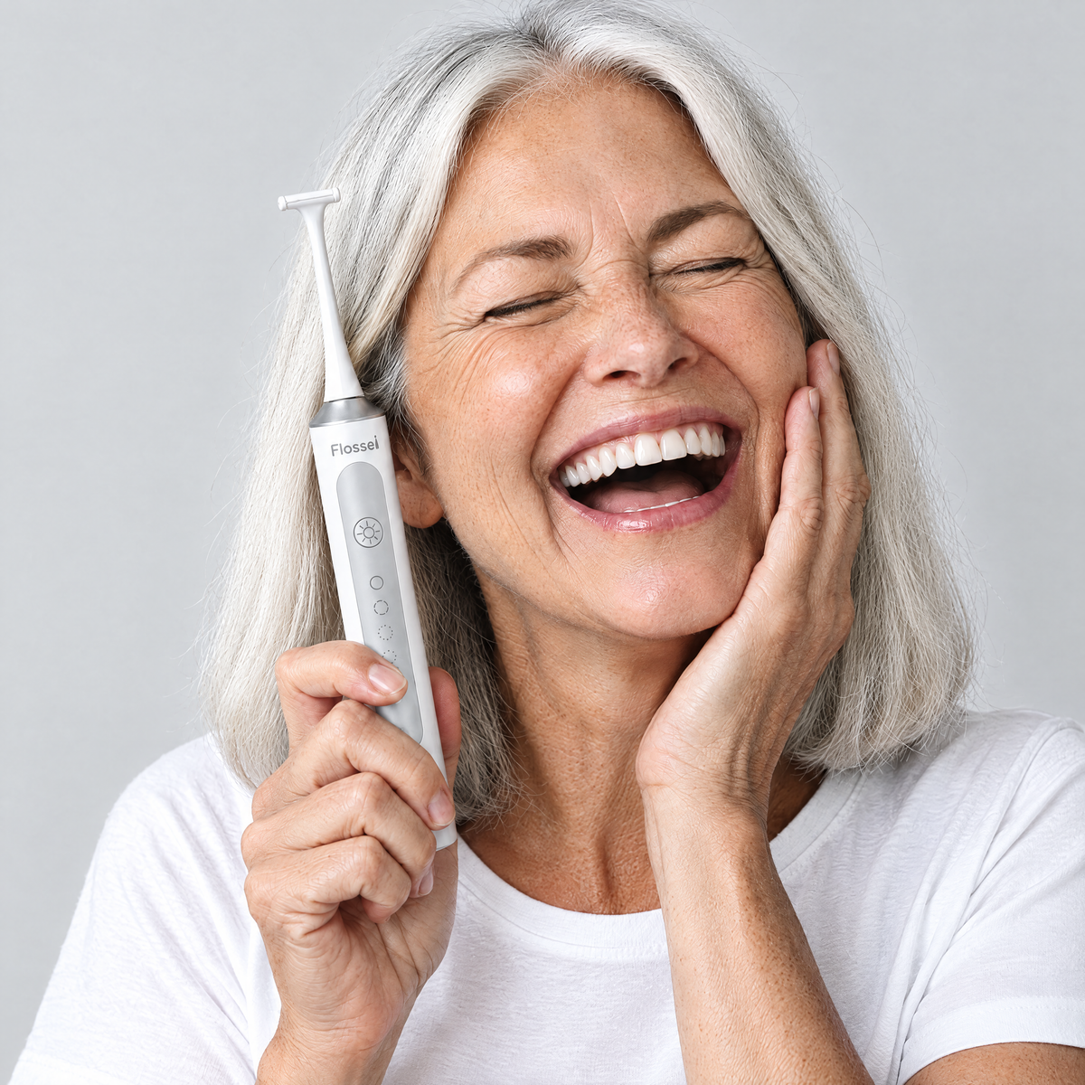 Smiling woman with silver hair holding the Flossei Electric Flosser in Arctic White beside her face
